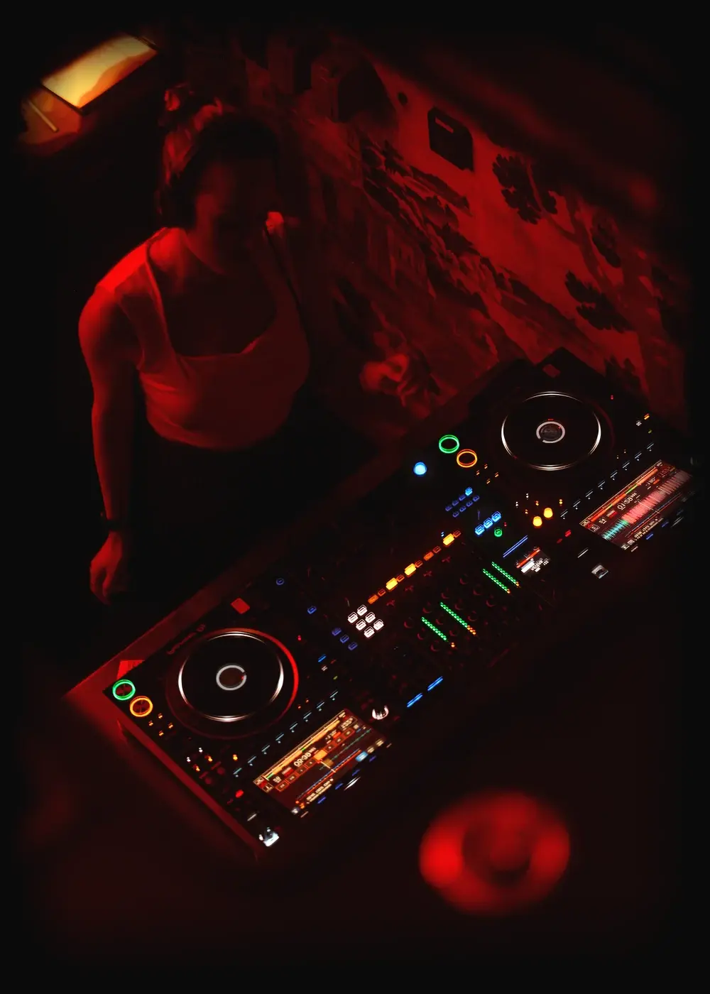 The DJ booth at Himitsu under red light, decks lit up against the hand-painted wall.
