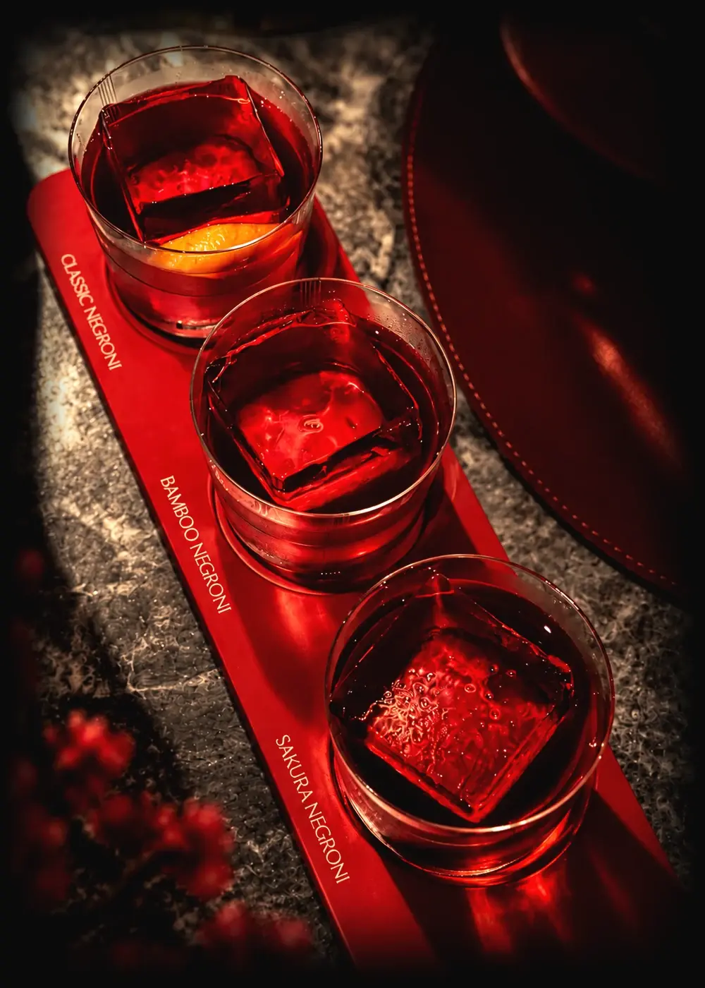 Three Negronis on a red serving board at Himitsu, marked Classic, Bamboo and Sakura, each over a single block of ice.