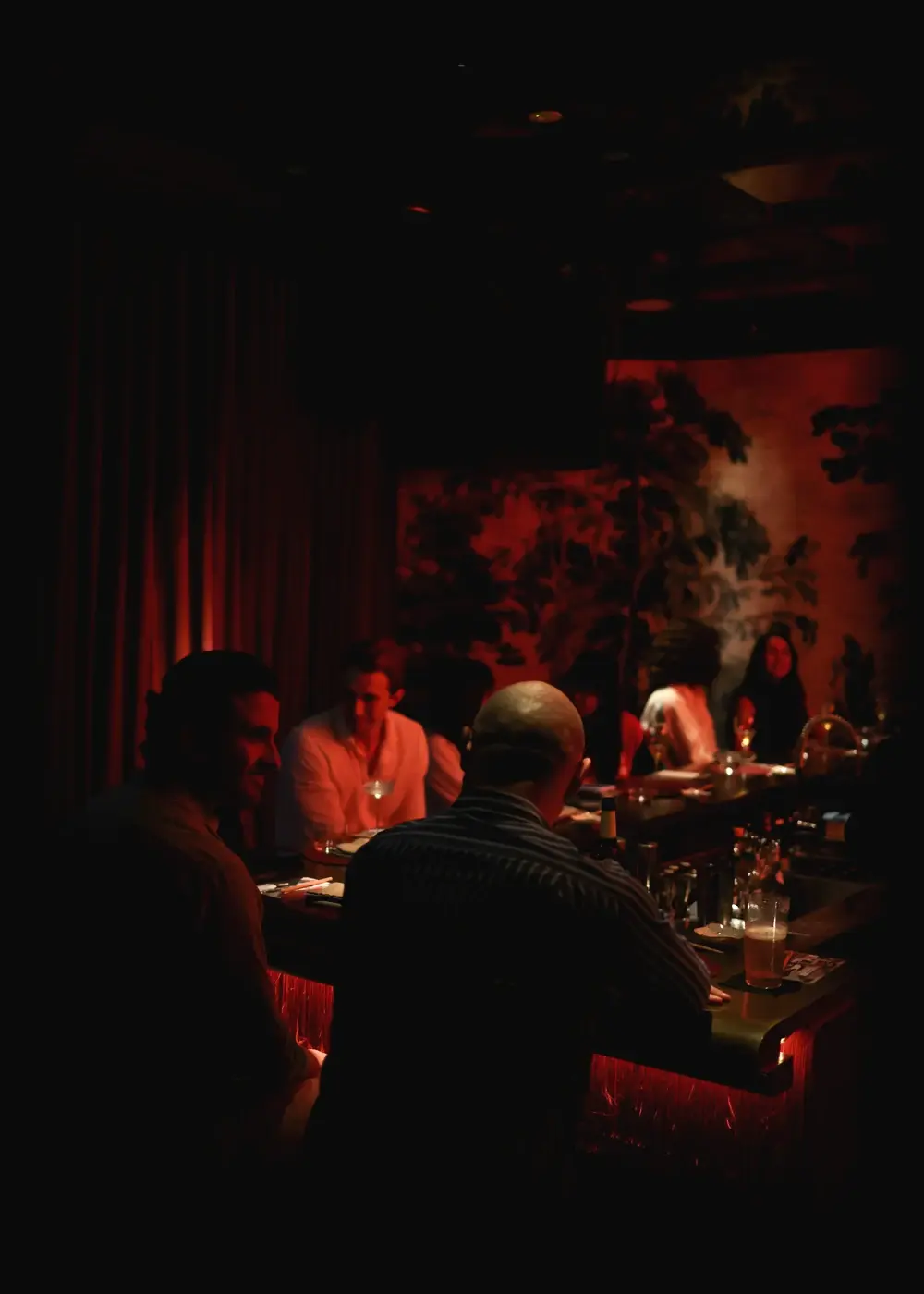 Guests along the lit counter at Himitsu in low red light, the hand-painted mural behind them.