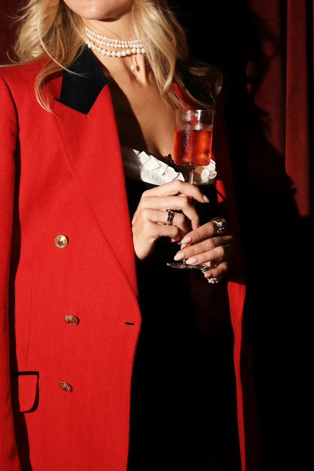 A guest wearing the red jacket at Himitsu, holding the Red Jacket cocktail against the bar’s red velvet curtain.
