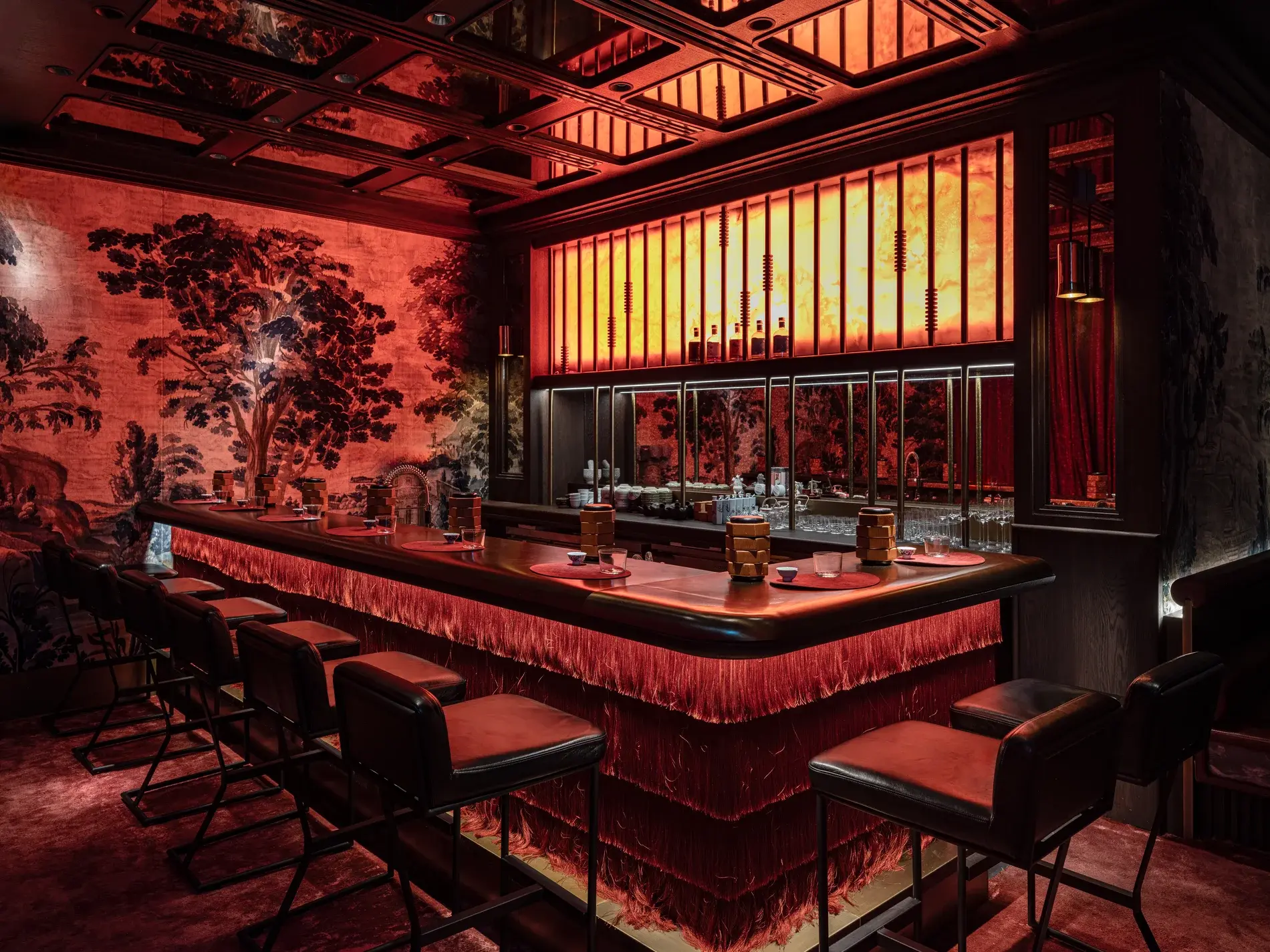 The Himitsu bar seen along its length: red banquettes, a hand-painted chinoiserie wall, and a lit spirits shelf behind the counter.