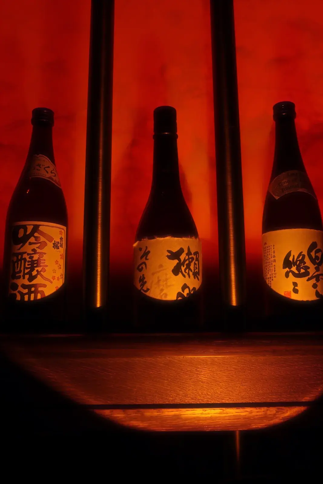 Three sake bottles standing in a row against panels of deep red light.